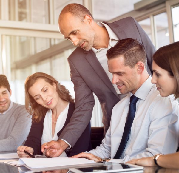 Team leader pointing at report during meeting with his colleagues. Business team working together in modern office. Young minds of office discussing new ideas for marketing with boss.